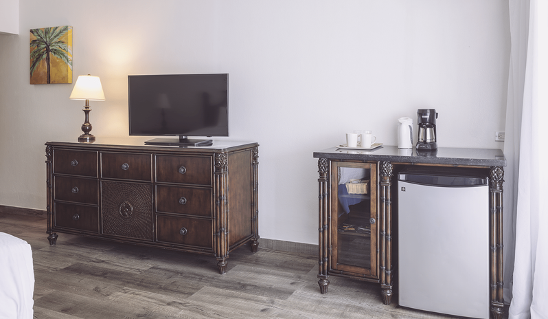 Premium Oceanview Partial Ocean View console area featuring a flat-screen television on a dark carved wood dresser and a mini fridge refreshment station with a coffee maker at St James’s Club & Villas by Kenwood Travel