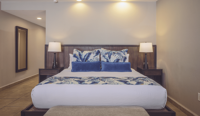 Royal Suite Bay View featuring tropical patterned pillows, dark wood headboard with nightstands, and bedside table lamps at St James’s Club & Villas by Kenwood Travel
