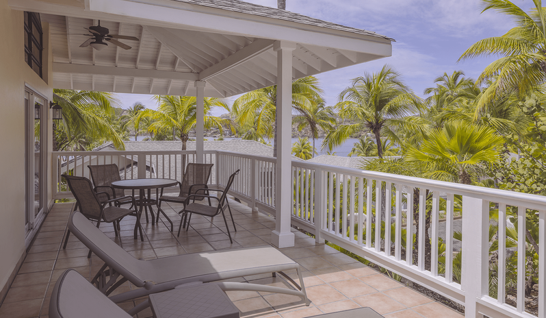 Two Bedroom Villa Spacious covered resort villa terrace with sun loungers, outdoor dining patio set, and views of tropical palm trees and the bay at St James’s Club & Villas by Kenwood Travel