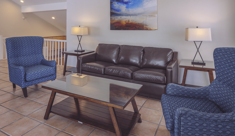 Two Bedroom Villa living area with a brown leather sofa, two blue patterned armchairs, a wooden glass-top coffee table, and table lamps at St James’s Club & Villas by Kenwood Travel