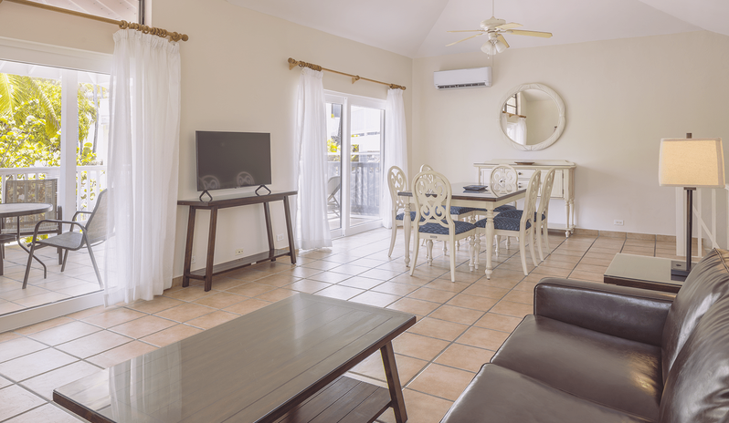Two Bedroom Villa living room with a leather couch and TV, dining table with chairs, vaulted ceilings, and patio access at St James’s Club & Villas by Kenwood Travel