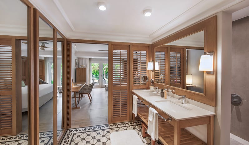Family Room bathroom featuring a wooden double vanity with dual sinks, large framed mirror, patterned tile floor, and louvered doors opening into the bedroom at Sugar Beach by Kenwood Travel