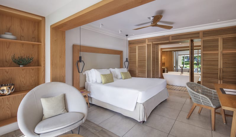 Premium Sea View Room king-size bed, rounded accent armchair, wooden built-in shelving, and louvered shutters opening into an ensuite bathroom with a freestanding tub at Sugar Beach by Kenwood Travel