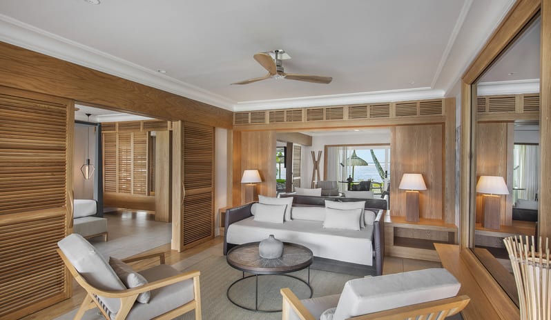 Executive Beach Front Suite modern daybed sofa, wooden accent armchairs, round coffee table, ceiling fan, and louvered wooden sliding partitions at Sugar Beach by Kenwood Travel