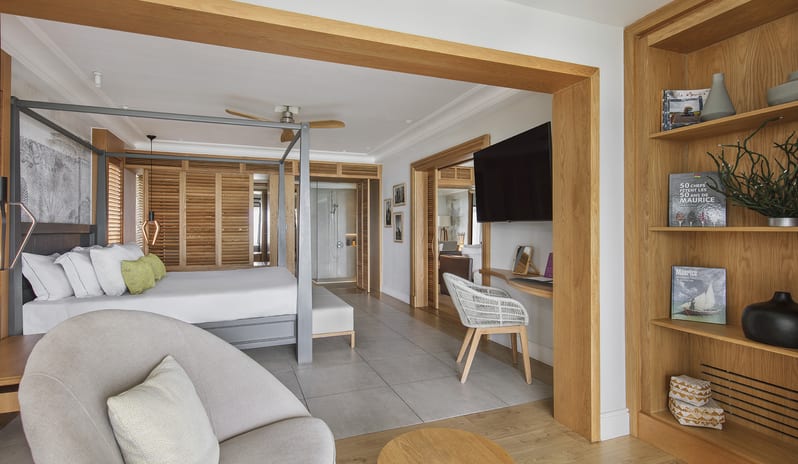 Executive Beach Front Suite lounge area into an executive beachfront hotel suite, featuring wooden built-in shelving, a modern canopy king bed, work desk, and wall-mounted TV at Sugar Beach by Kenwood Travel