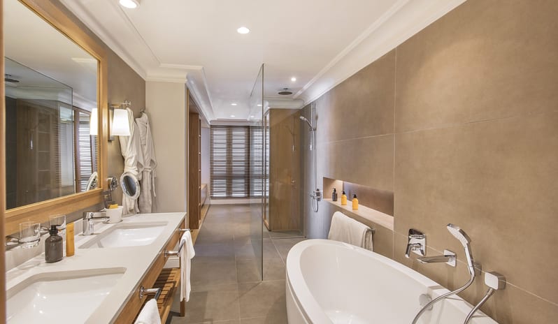 Executive Beach Front Suite bathroom in an executive beachfront suite featuring a freestanding soaking tub, glass-enclosed walk-in shower, double vanity sinks, and wood-framed mirror at Sugar Beach by Kenwood Travel