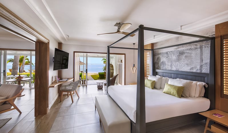 Executive Beach Front Suite four-poster canopy king bed with plush pillows, wall-mounted TV, work desk, and sliding doors opening directly to a patio and ocean view at Sugar Beach by Kenwood Travel