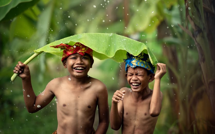 Indonesian Asian children wear traditional headdresses and sarongs, playing rain water and using banana leaves with fun..jpg
