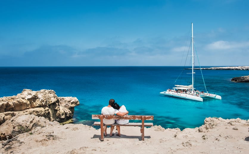 Loving couple sitting on a bench and looks at the lagoon. Honeymoon lovers. Man and woman on the island. Couple in love on vacation. A voucher for a cruise trip. Sea tour. Honeymoon trip. Cruise ship.jpg